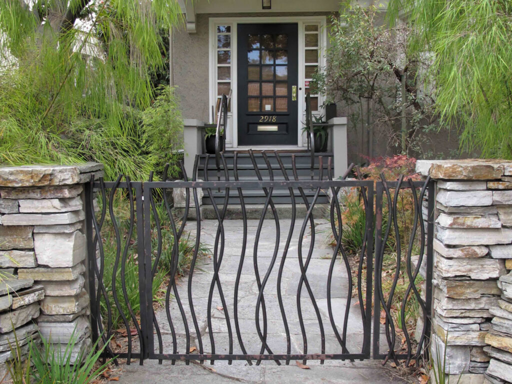 A decorative metal gate with wavy vertical bars and stone pillars, installed by Ozark Fence in Lakewood, CO.