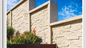 A decorative concrete fence with a stone-like texture under a blue sky by StackWall Manufacturing in Pomona, CA.
