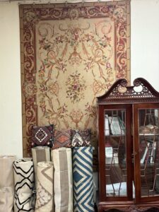 A decorative wall tapestry and rolled rugs displayed in the showroom of Woven Treasures, Inc in Mobile, AL.