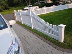 A decorative white picket fence bordering a paved driveway, expertly installed by Zelaya Fence in New York City, NY.