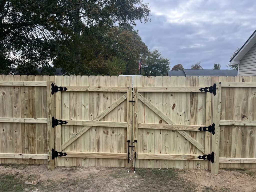 A close-up of a newly installed wooden double gate with decorative black hinges by Fencingphd.nc in Fayetteville, NC.