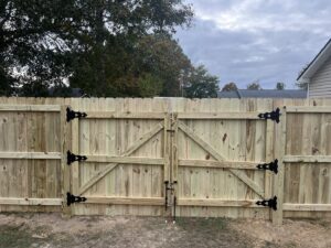 A close-up of a newly installed wooden double gate with decorative black hinges by Fencingphd.nc in Fayetteville, NC.