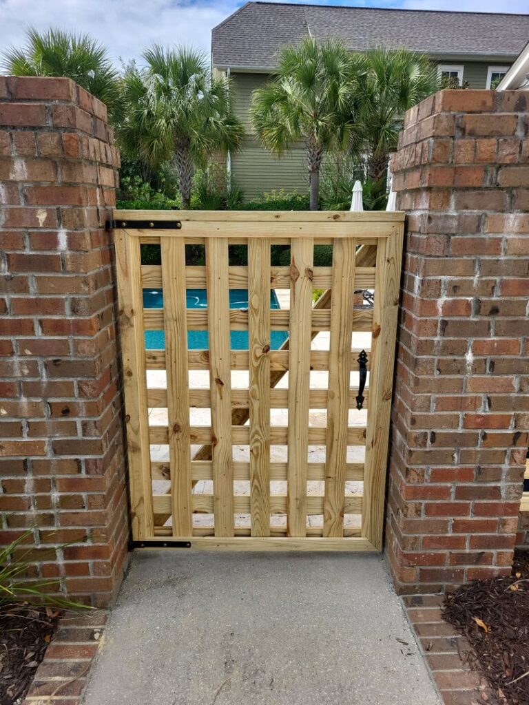 A decorative wooden gate installed within a brick wall by JB FENCE Brothers company llc in North Charleston, SC.