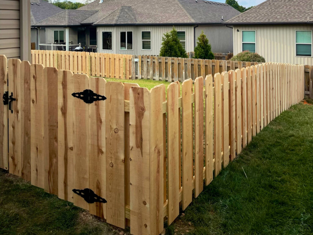 A newly installed decorative wood privacy fence with a gate and scalloped tops by Axiom Fence LLC in Springfield, MO.