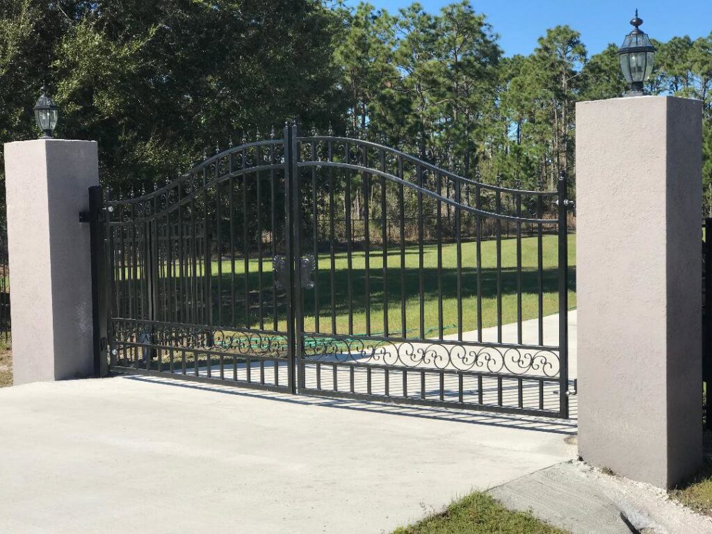 A decorative wrought iron entry gate with sturdy stone pillars, expertly installed by Fencing & Railing 2 Corp in Orlando, FL.