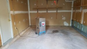 A large dehumidifier operating in a garage for water damage restoration by My Carpet Cleaning & Restoration Services in Silver Spring, MD.