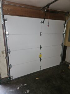 A close-up of a dented or damaged garage door panel at the bottom, showing a common repair job by Alliance Overhead Garage Doors Inc. in Portland, OR.