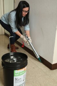 A Detourgel technician applying pest control gel with a large caulk gun, with a product bucket nearby in Whittier, CA.