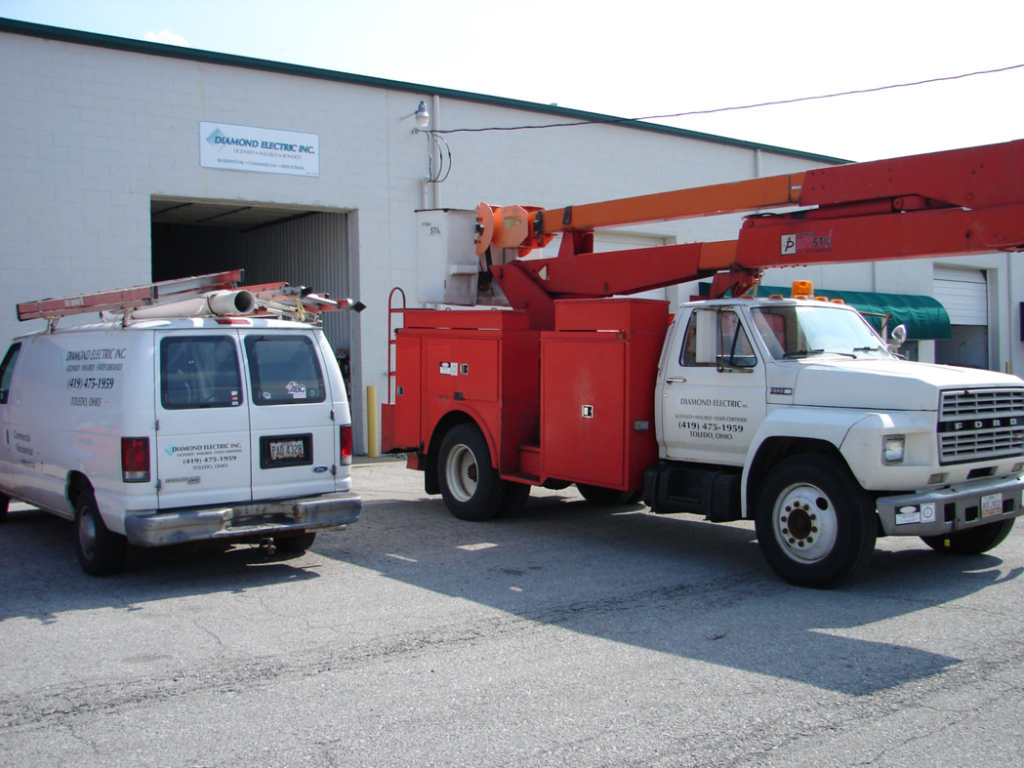A Diamond Electric service van and a red bucket truck parked outside a commercial building in Toledo, OH.