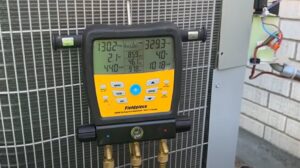 A digital manifold gauge set connected to an outdoor AC unit showing readings by RESTQ HVAC Repairs & Services in Rockville, MD.