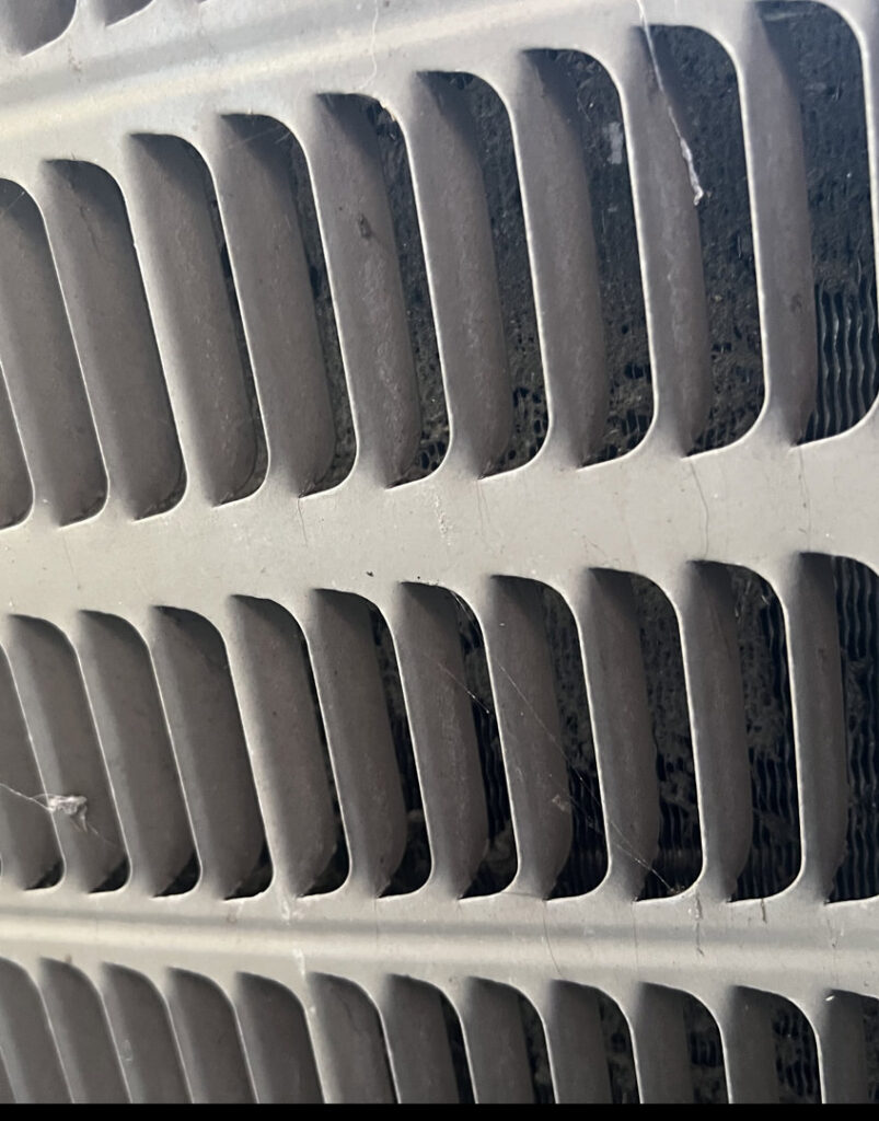 A close-up view of a dirty outdoor AC condenser coil, indicating a need for maintenance by American Team Inc in Warminster, PA
