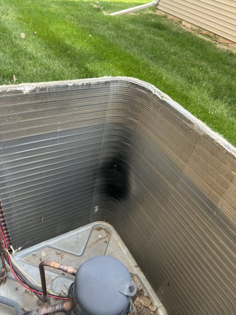 A close-up view of dirty AC condenser coils, indicating a need for cleaning by Omega Air Solutions in West Des Moines, IA.