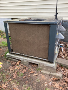 An outdoor AC unit with a side panel removed, revealing a very dirty coil, ready for cleaning by Your Angel Heating And Cooling LLC in Cary, NC.