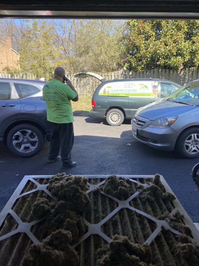 A dirty air filter in the foreground with a Clean Air Solutions technician in the background in Gaithersburg, MD.