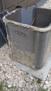 A close-up view of a dirty and damaged outdoor AC condenser coil needing repair from Arrowseal of Billings HVAC in Billings, MT.