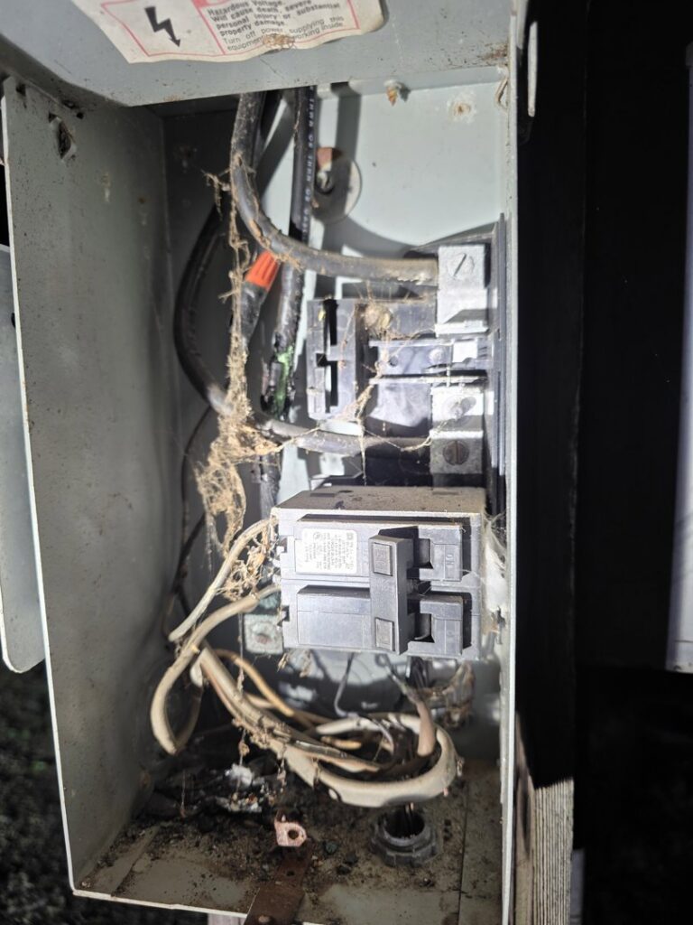 A dirty and possibly damaged outdoor electrical panel with exposed wires, requiring service from Titus & Son's Electric in Bluffton, IN.