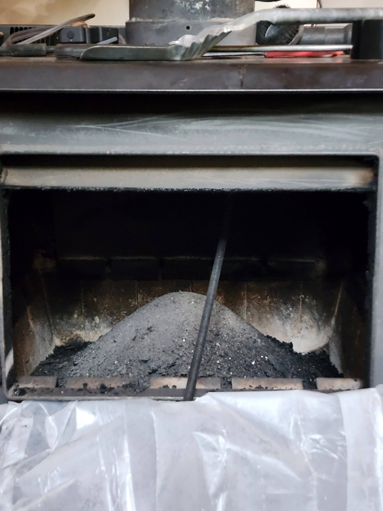 A dirty fireplace with a large pile of ash and soot, indicating a need for chimney sweep services by Chimney Wizards LLC in Orofino, ID.