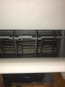 Close-up view of dirty heat pump coils inside a mini-split unit before cleaning by Winks Heat Pump Cleanings in Bangor, ME