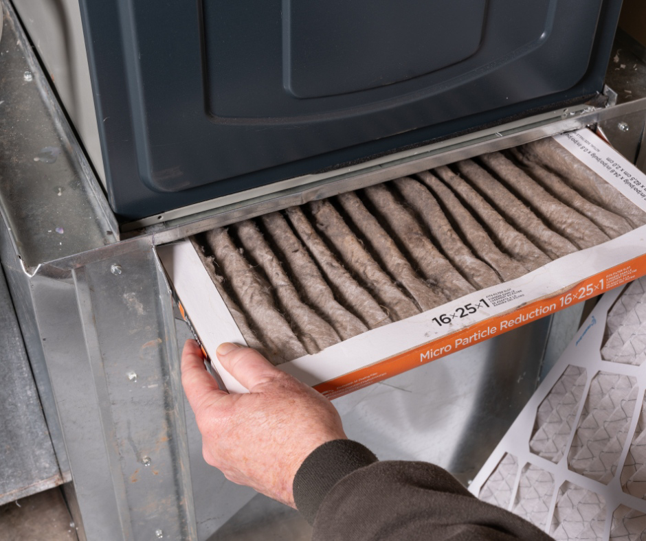A hand replacing a dirty HVAC air filter in a furnace at a home serviced by M Heating & Cooling, Inc. in Green Bay, WI