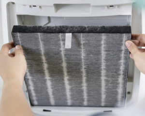 Hands removing a very dirty HVAC air filter, indicating a need for replacement or cleaning by Uptack in Haverhill, MA.