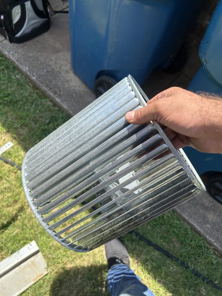 A dirty HVAC blower wheel held by a technician, indicating cleaning or replacement service by Oklahoma Climate Solutions in Oklahoma City, OK.
