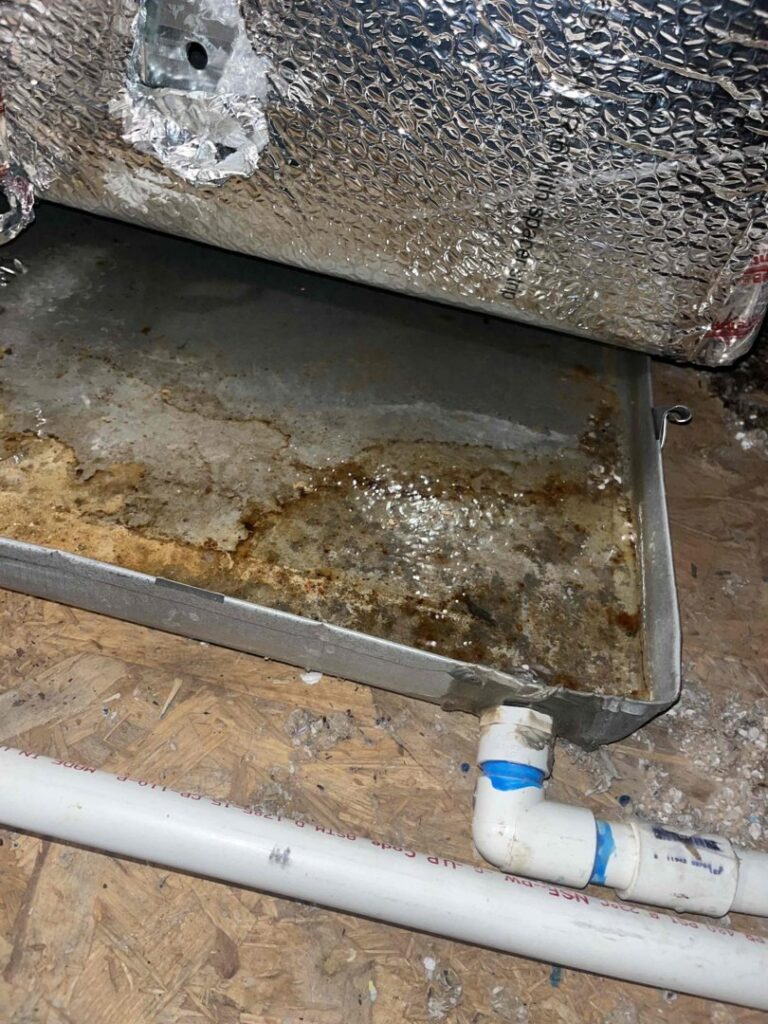 A dirty HVAC condensate pan with a PVC drain line, indicating a service need by Steadfast Mechanical in Gilbert, AZ.