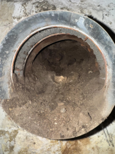 A close-up view of a dirty, debris-filled HVAC duct or flue opening needing service from All Points HVAC in Worcester, MA.