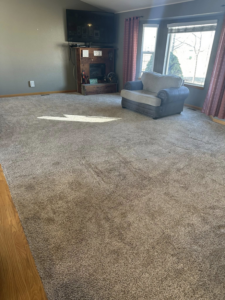 A living room with a visibly dirty, light brown carpet before professional cleaning by North Colorado Kwik Dry Total Cleaning in Johnstown, CO.