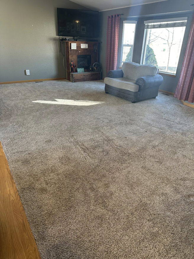 A living room with a visibly dirty, light brown carpet before professional cleaning by North Colorado Kwik Dry Total Cleaning in Johnstown, CO.