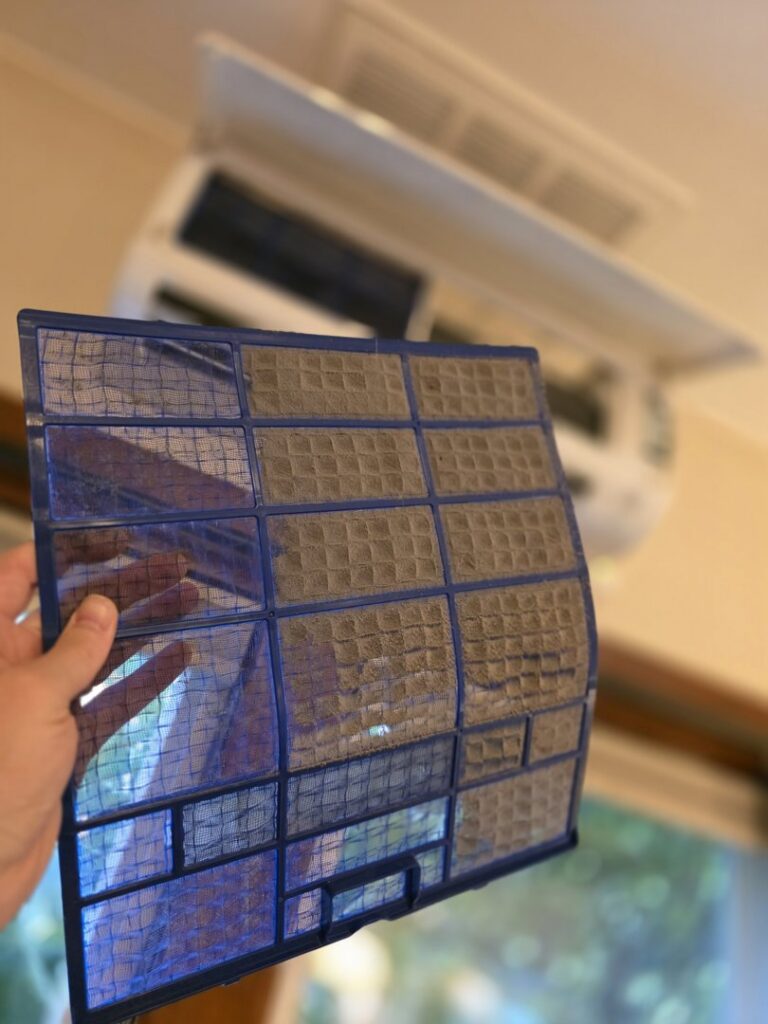 A dirty mini-split air filter being removed for cleaning or replacement by Best Heat & Air in Tacoma, WA.