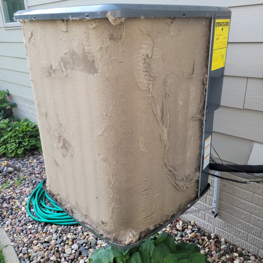 An extremely dirty outdoor AC condenser unit requiring cleaning by Trade Allies Heating and Cooling in Ankeny, IA.