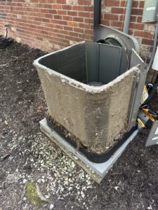 A heavily soiled outdoor AC unit covered in dirt and debris, indicating a need for cleaning by Radiant Heating & Cooling in Fishers, IN.