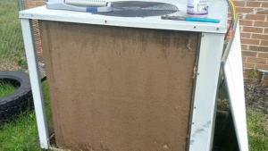 A dirty outdoor HVAC condenser unit with tools on top, ready for cleaning or service by Conway's Heating & Air in Concord, NC.