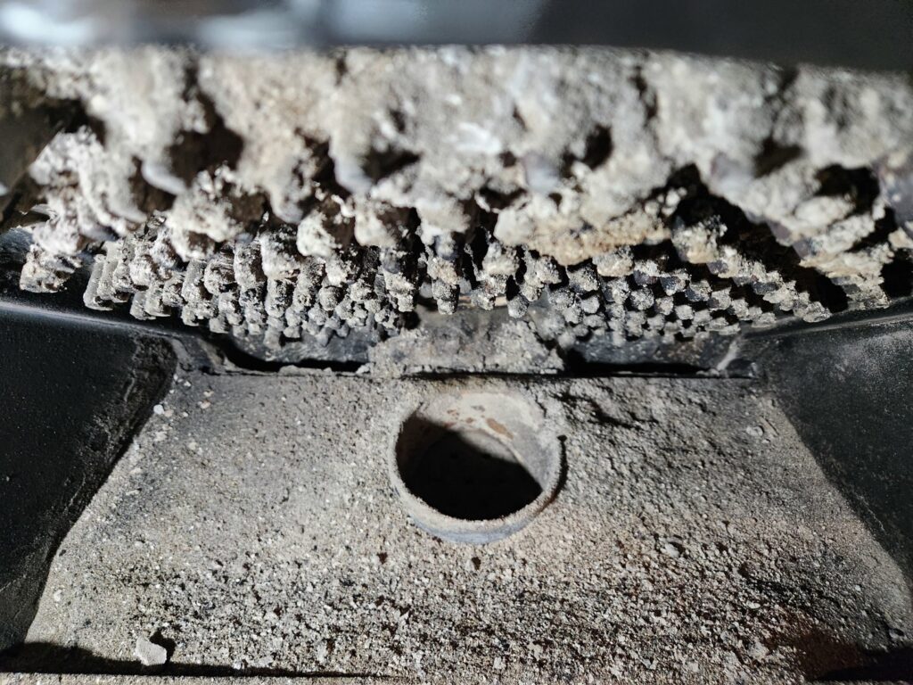 Close-up of a dirty pellet stove burn pot with significant creosote buildup, requiring cleaning by Top Dog Hearth Repair & Maintenance, LLC in Worcester, MA