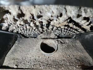 Close-up of a dirty pellet stove burn pot with significant creosote buildup, requiring cleaning by Top Dog Hearth Repair & Maintenance, LLC in Worcester, MA