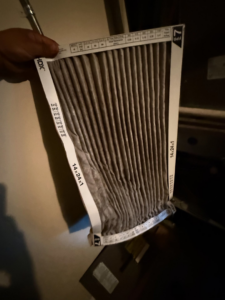 A hand holding a dirty, used HVAC air filter (14x24x1) removed during a service by GUS' HVAC Services in Canton, GA.
