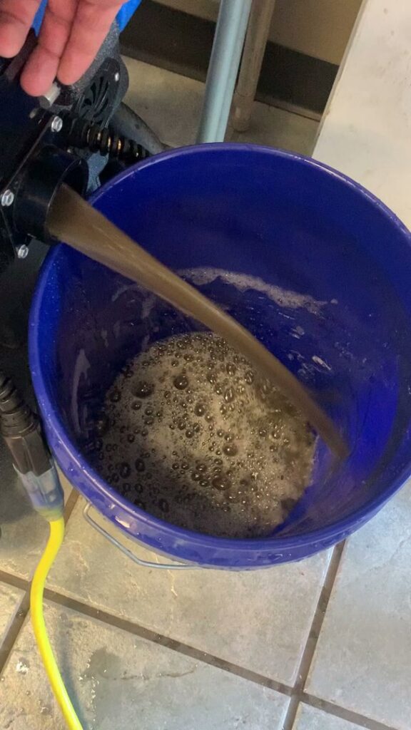 Dirty water being extracted into a blue bucket, demonstrating effective carpet and upholstery cleaning by Good Guys Carpet Cleaning in Katy, TX.