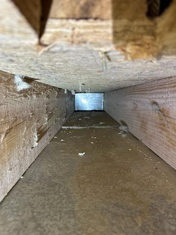 A view inside a dirty wooden air duct with accumulated debris, before cleaning by Vacman Air Duct Cleaning in South Bend, IN