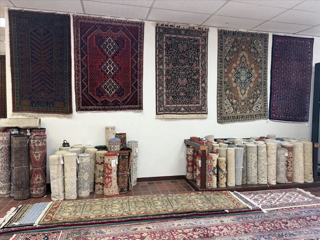 A diverse collection of rugs, both rolled and hanging, showcased in the showroom of Woven Treasures, Inc in Mobile, AL.