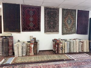 A diverse collection of rugs, both rolled and hanging, showcased in the showroom of Woven Treasures, Inc in Mobile, AL.