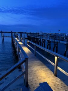 A wooden dock illuminated by pathway lighting at dusk, showcasing outdoor electrical installation by New York Electrical Design in Freeport, NY