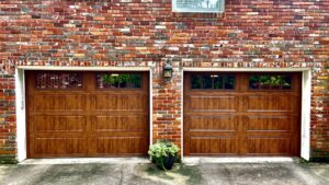 Two elegant brown garage doors with decorative windows installed on a brick house by The Birmingham Man Garage Doors in Birmingham, AL.