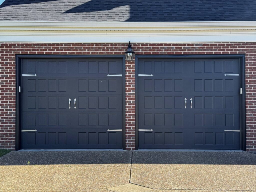 Two dark grey garage doors with decorative hardware installed on a brick home by Precision Garage Door of Owensboro Evansville in Owensboro, KY.