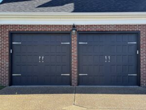 Two dark grey garage doors with decorative hardware installed on a brick home by Precision Garage Door of Owensboro Evansville in Owensboro, KY.