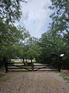 A double metal entry gate installed in a wooded area by ProScape Outdoor Construction LLC in Norman, OK.