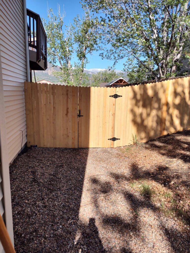 A newly installed wood fence with a double gate next to a residential building, completed by Good Neighbor Fencing, LLC in Colorado Springs, CO.