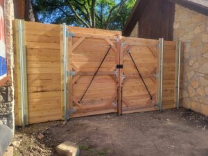 A newly installed double wooden gate with sturdy metal bracing, next to a stone wall, by QD & E Fencing in Fort Worth, TX.