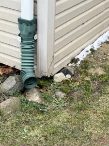 A downspout extension near a house foundation with damaged siding, a pest risk addressed by Ramer Pest Control in Fort Wayne, IN.