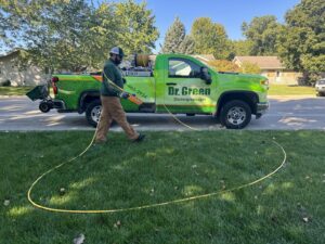 A Dr. Green Services employee applying pest control treatment to a lawn from a branded truck in Joliet, IL