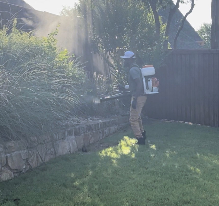 A Dr. Green Services employee applying pest control treatment with a backpack sprayer to shrubs and lawn edges in Joliet, IL